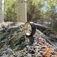 men's gold wedding ring with carbon fiber on a boulder