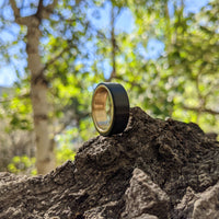 men's gold wedding ring with carbon fiber balanced on a rock